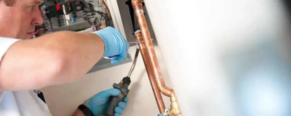 Water heater repair technician testing copper pipe connections and controls in Oakland, CA